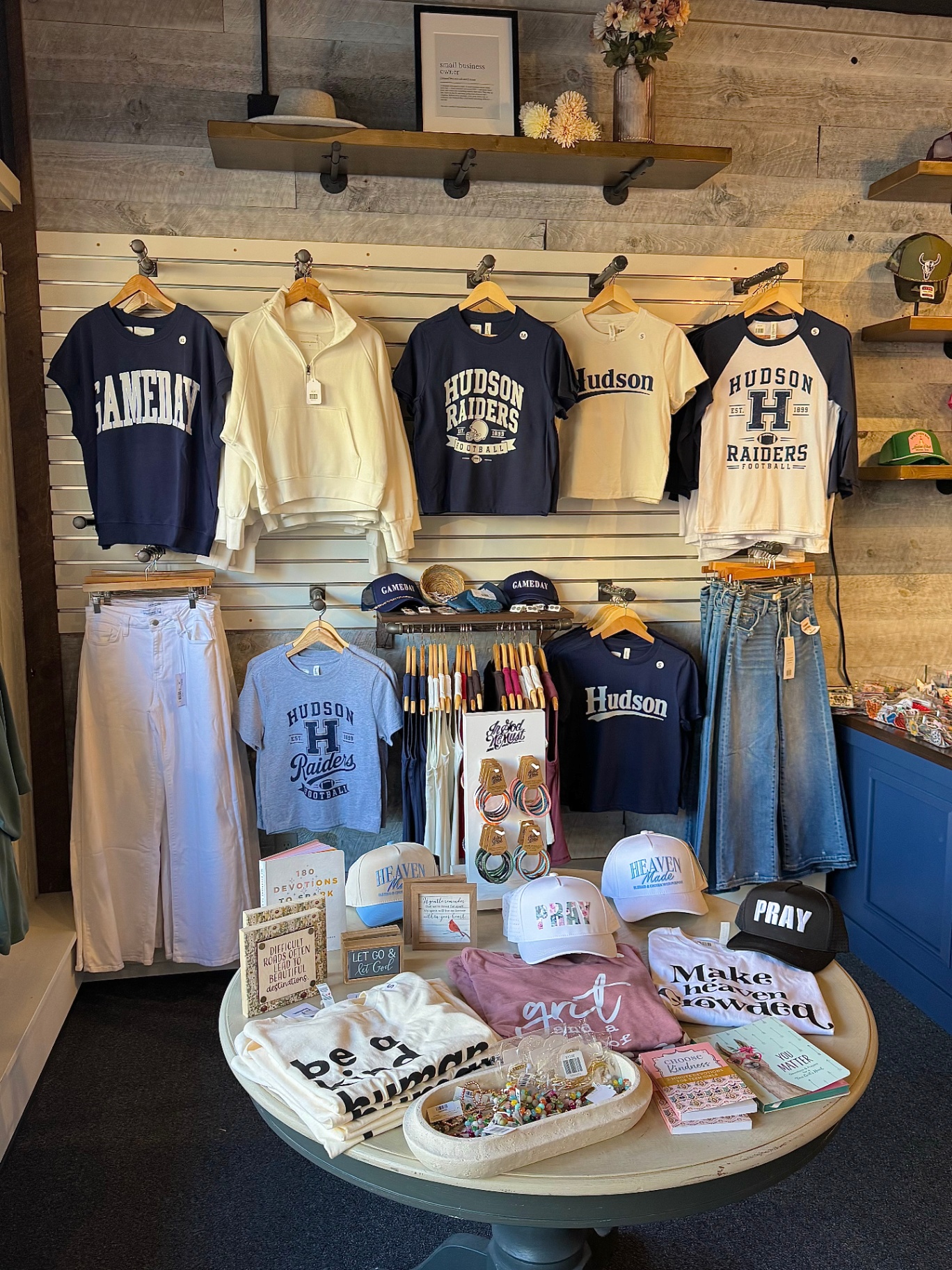 Hudson Raiders gameday tees, caps, and denim styled on a display wall and table